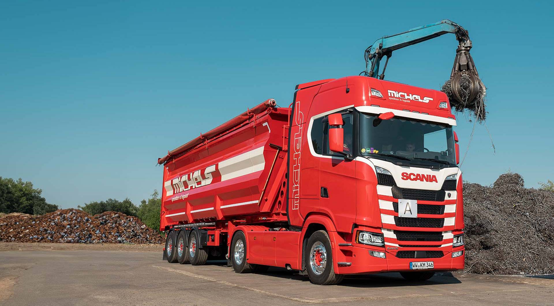 Roter Lkw mit Kran und Mulde.