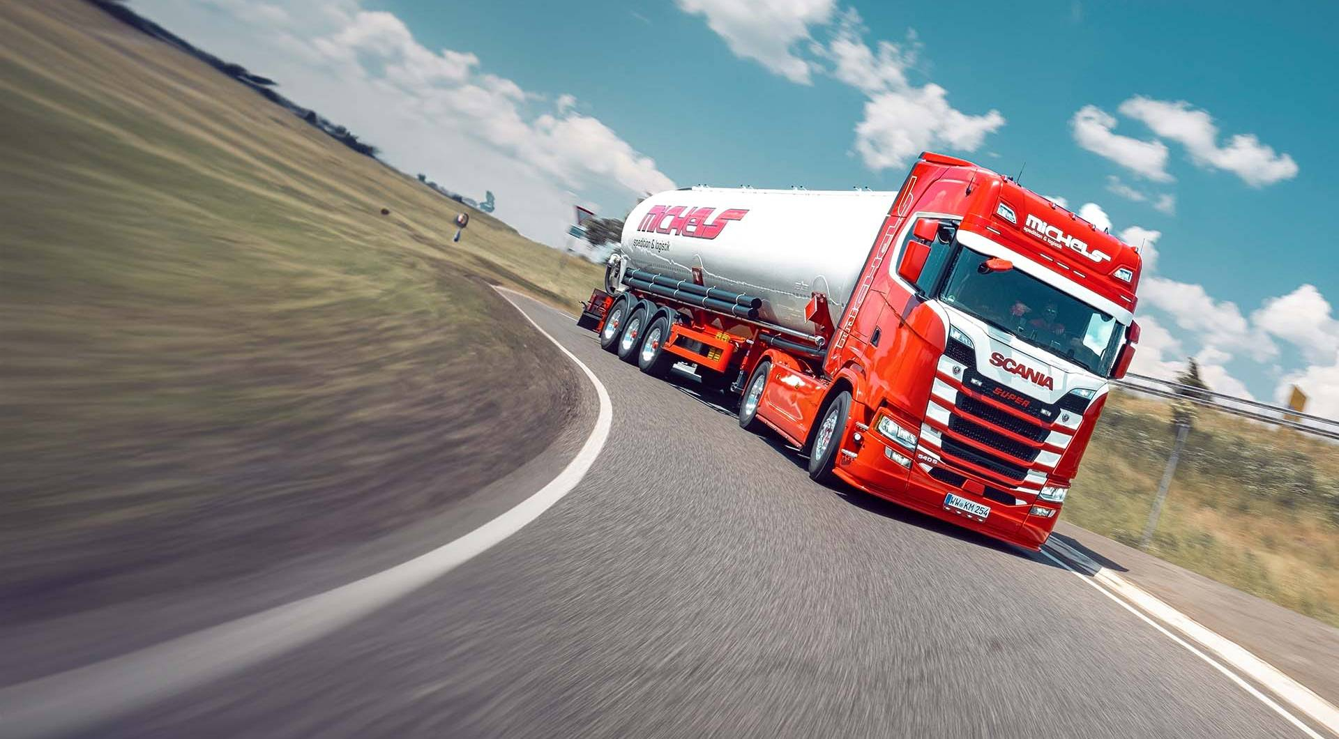Roter Lkw mit Tankanhänger auf kurviger Straße.